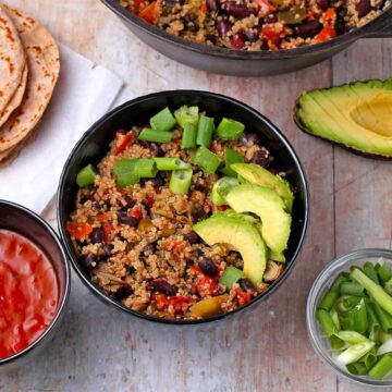 A bowl of Southwestern beans and quinoa with sliced avocado and scallions.