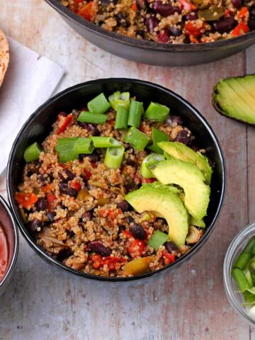 A bowl of Southwestern beans and quinoa with sliced avocado and scallions.