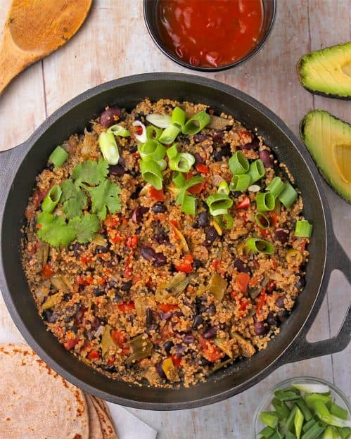 Southwestern beans and quinoa cooked in a black pan with cilantro and sliced scallions.