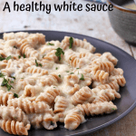 Vegan bechamel (white) sauce over whole wheat curly pasta on a black plate.