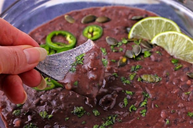 Refried black beans are spread on a tortilla with a spoon.