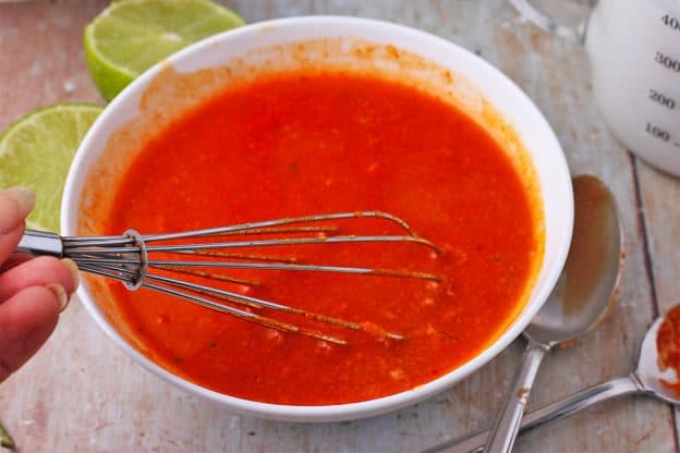 Satay sauce with Thai red curry paste, peanut butter, and vegetable broth is mixed in a white bowl with a whisk.