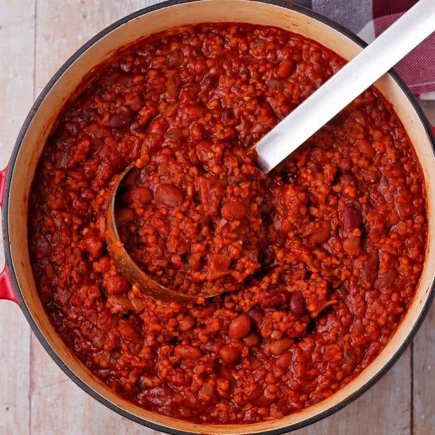 A soup pot is filled with plant-based chili with a ladle.