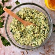Artichoke pesto with green parsley in a glass bowl with a small wooden spoon.