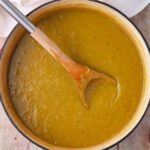 A soup pot filled with vegan split pea soup with a wooden spoon.