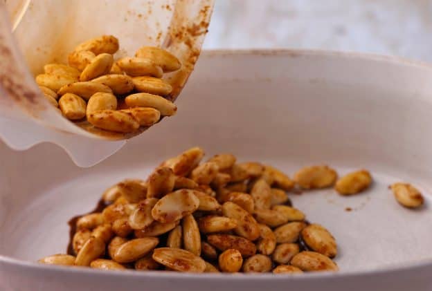 Blanched almonds are coated with Chinese 5-spice powder, soy sauce and agave syrup and are poured into a white baking dish.