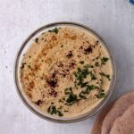 oil-free hummus in a bowl is garnished with sumac, ground cumin, and chopped parsley.