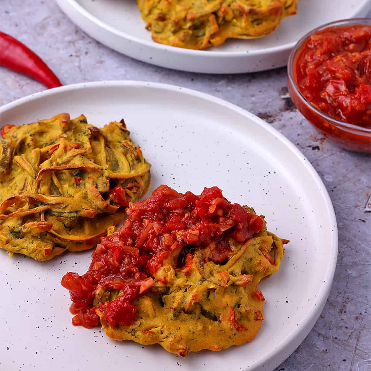 A white plate with baked pakoras with tomato chutney.