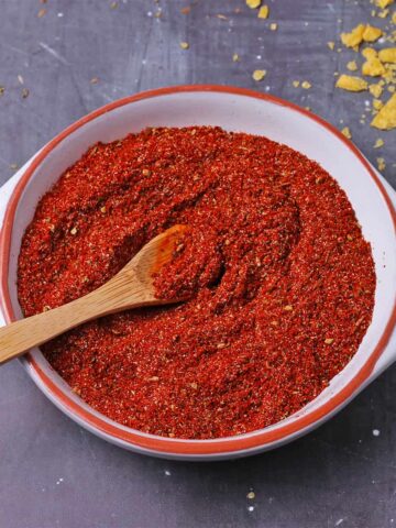 A white bowl is filled with homemade chili powder with a small wooden spoon.