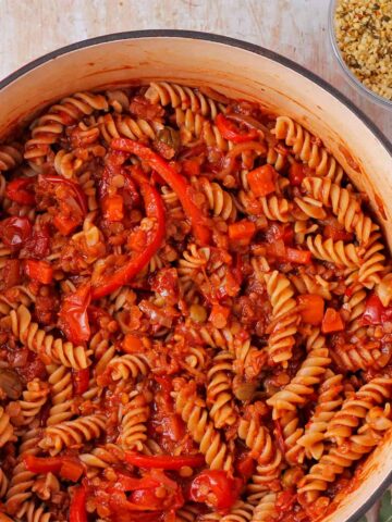 Cooked pasta is made with lentils cacciatore with capers, tomatoes, and red pepper slices.