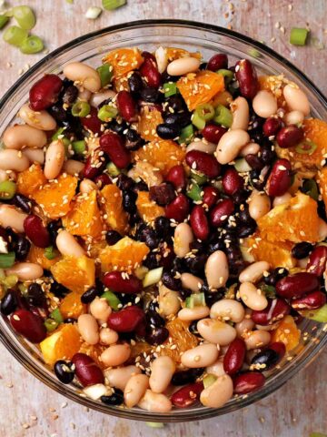 A bowl with 3-bean salad, with fresh orange cubes, sesame seeds, and scallions.