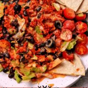 A plate with taco salad filled with bulgur taco meat, black beans, lettuce, tomatoes, black olives, avocados, tortilla chips, and dressing.
