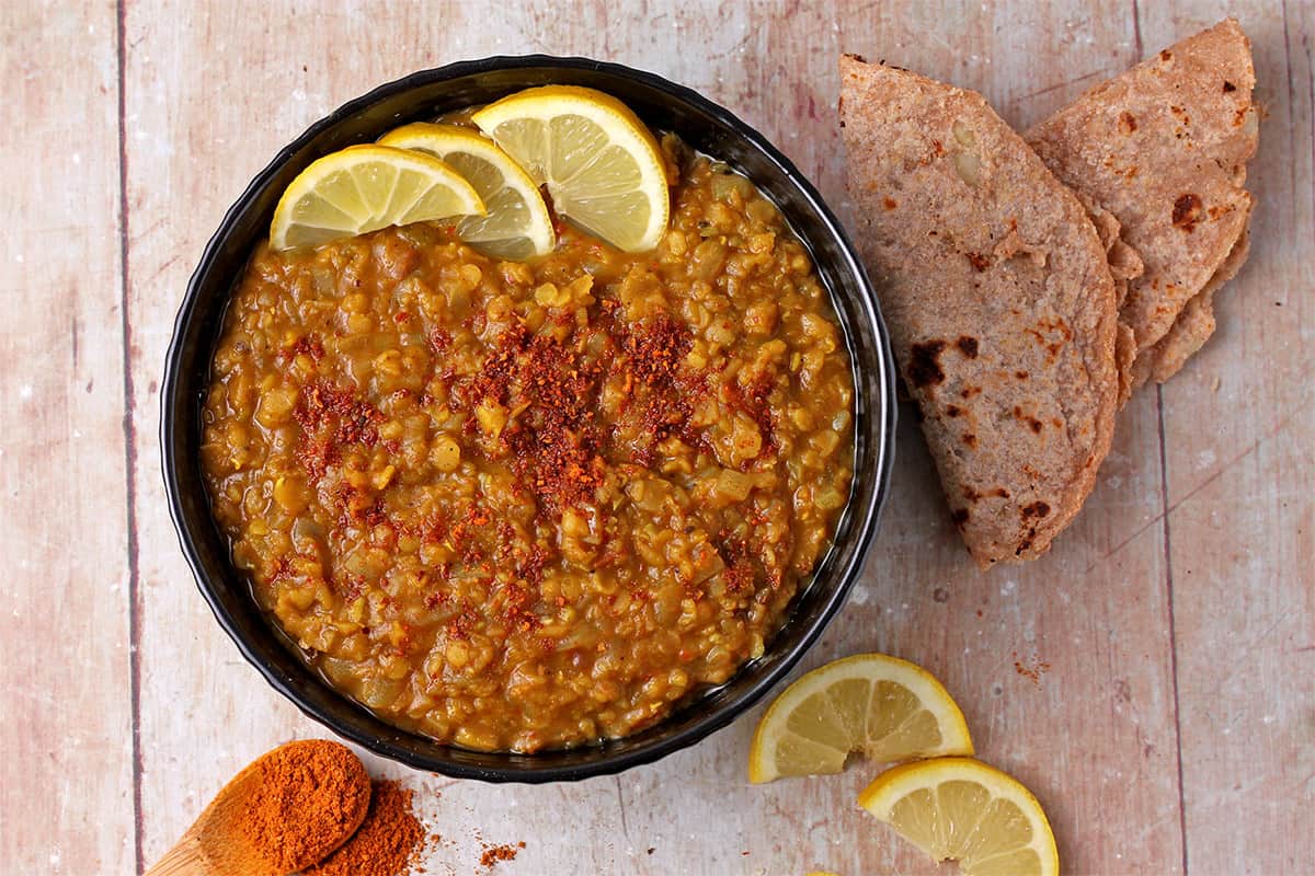 An overhead of a bowl filled with red lentil stew with Berbere spice blend and lemon slices.