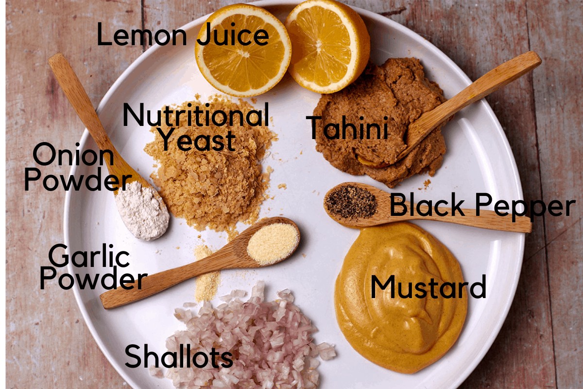 A plate with minced shallots, mustard, black pepper, tahini, lemons, nutritional yeast, onion powder, garlic powder, and black pepper.