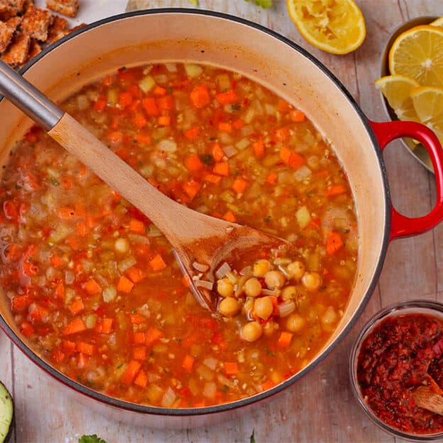A pot of soup with chickpeas, onions, carrots, and a dish of harissa paste.