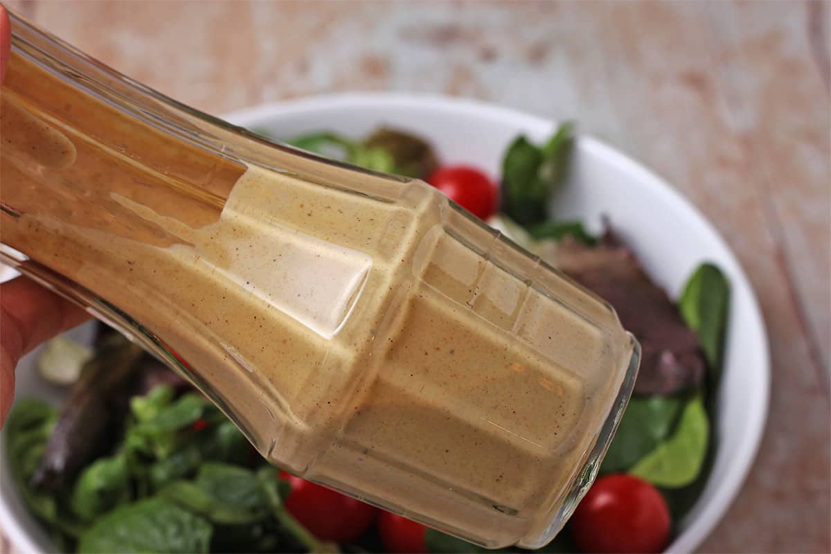 Mustard tahini dressing is shaken in a bottle.
