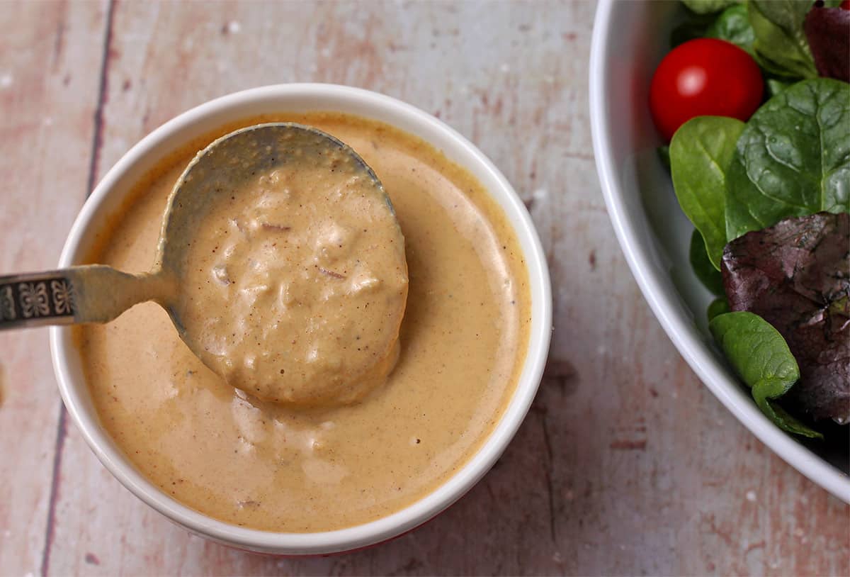 Overhead shot of mustard tahini dressing in bowl and in small ladle.