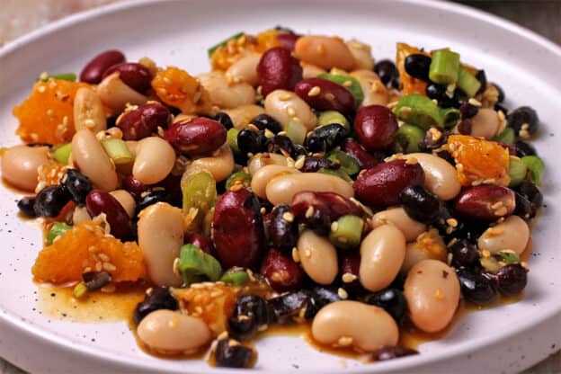 A plate with white beans, black beans, red kidney beans, oranges, scallions, and sesame seeds.