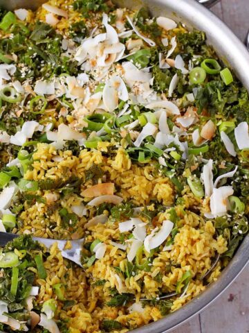 Turmeric rice in a skillet with coconut flakes, sesame seeds, kale, and scallions.