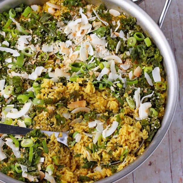 Turmeric rice in a skillet with coconut flakes, sesame seeds, kale, and scallions.