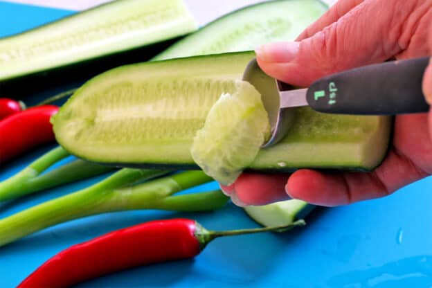 The seeds of a cucumber are removed using a spoon.