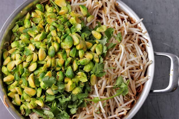 Brussels sprouts cut into quarters, mung bean sprouts and cilantro in a skillet.