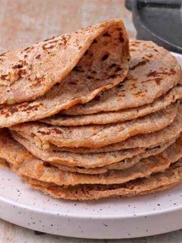 Whole wheat potato tortillas are stacked on a white plate and the top tortilla is folded over.