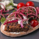 A pita bread with vegan koftas, aioli, pickled red onions and parsley, lettuce, tomatoes, and cucumber.