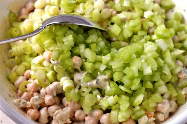 Diced celery and scallions are mixed into a bowl of chickpeas with creamy dressing.