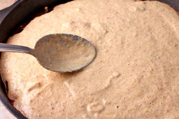 Cornmeal batter is spread with a spoon over vegan tamale pie filling.