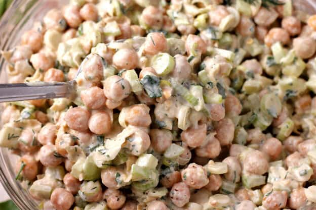 A close up view of chickpea salad with cashew cream dressing, diced celery, scallions, and fresh dill and parsley.