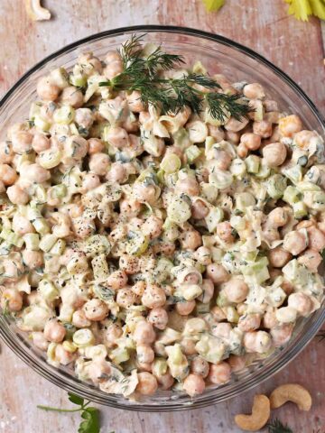 Creamy vegan chickpea salad in a glass bowl with fresh dill stalks as a garnish.