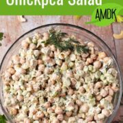 Creamy chickpea salad with ground pepper, fresh dill, celery, and scallions in a glass bowl.