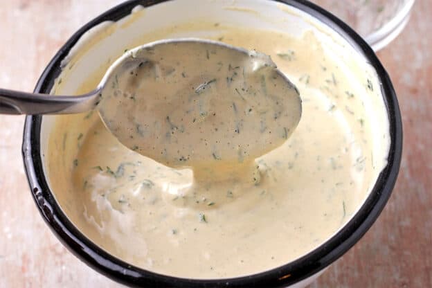 Cashew dressing with fresh herbs in a white bowl with a spoon.