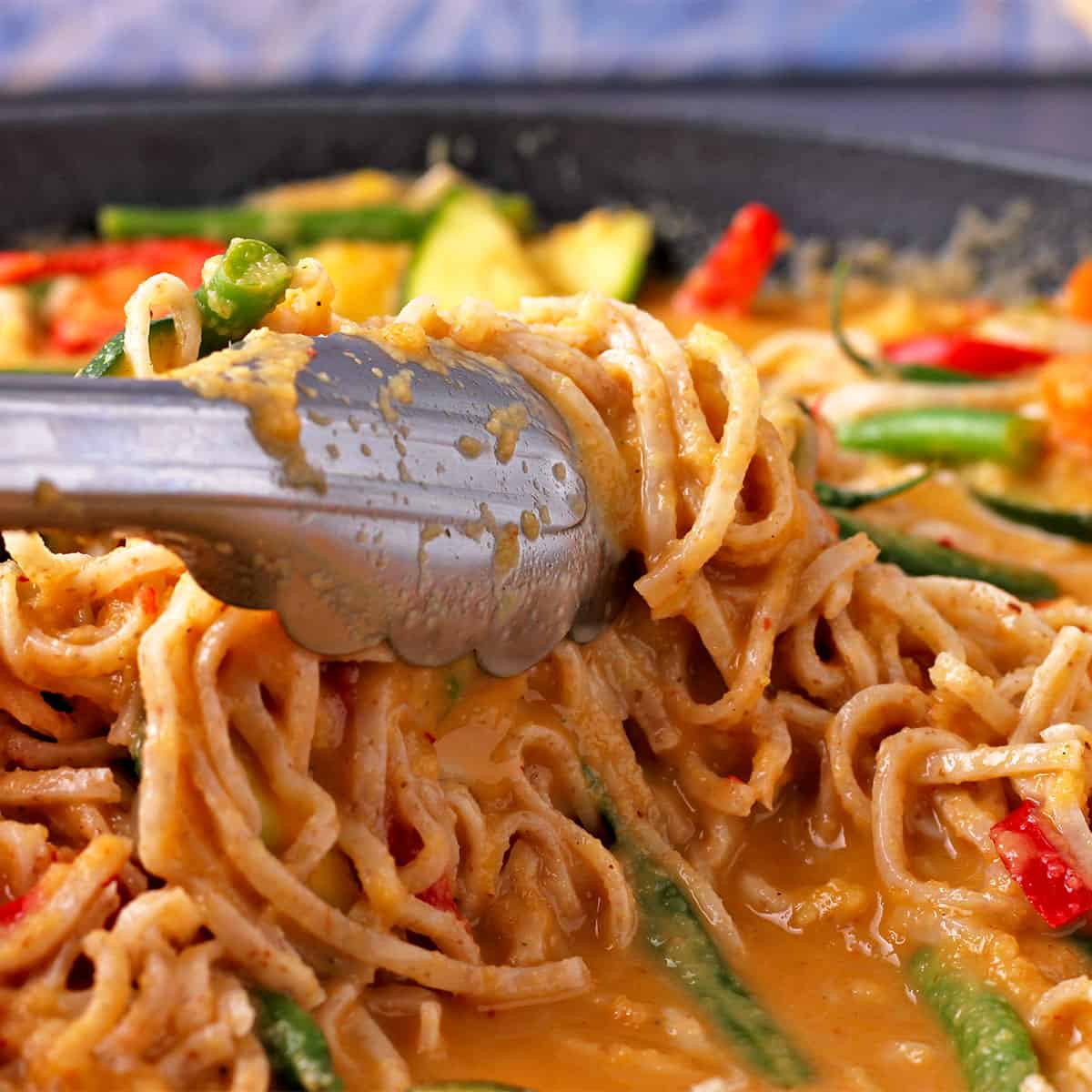 Noodles are stirred into a bowl of vegetable mango curry.