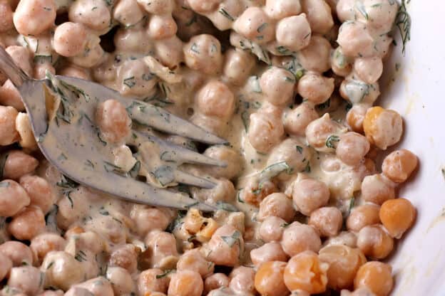 Chickpeas are mashed into dressing with a fork.