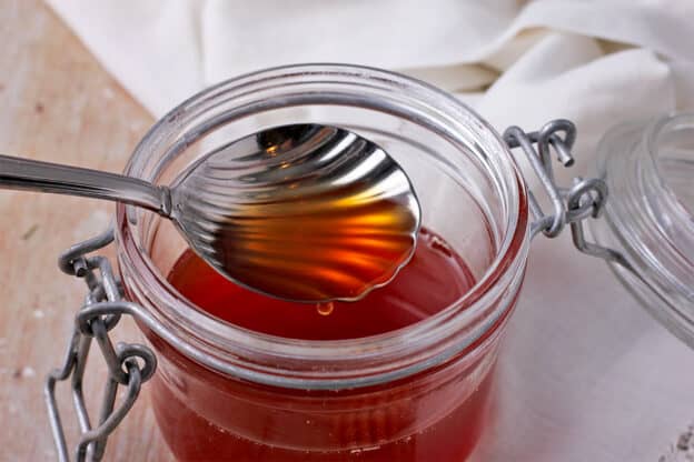 Vegan honey is held in a spoon over a jar of honey.