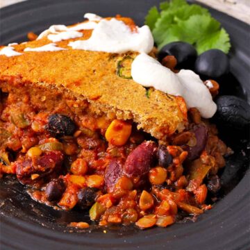 Vegan tamale pie recipe with cornbread bread topping and vegan sour cream on a black plate.