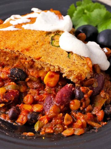 Vegan tamale pie recipe with cornbread bread topping and vegan sour cream on a black plate.