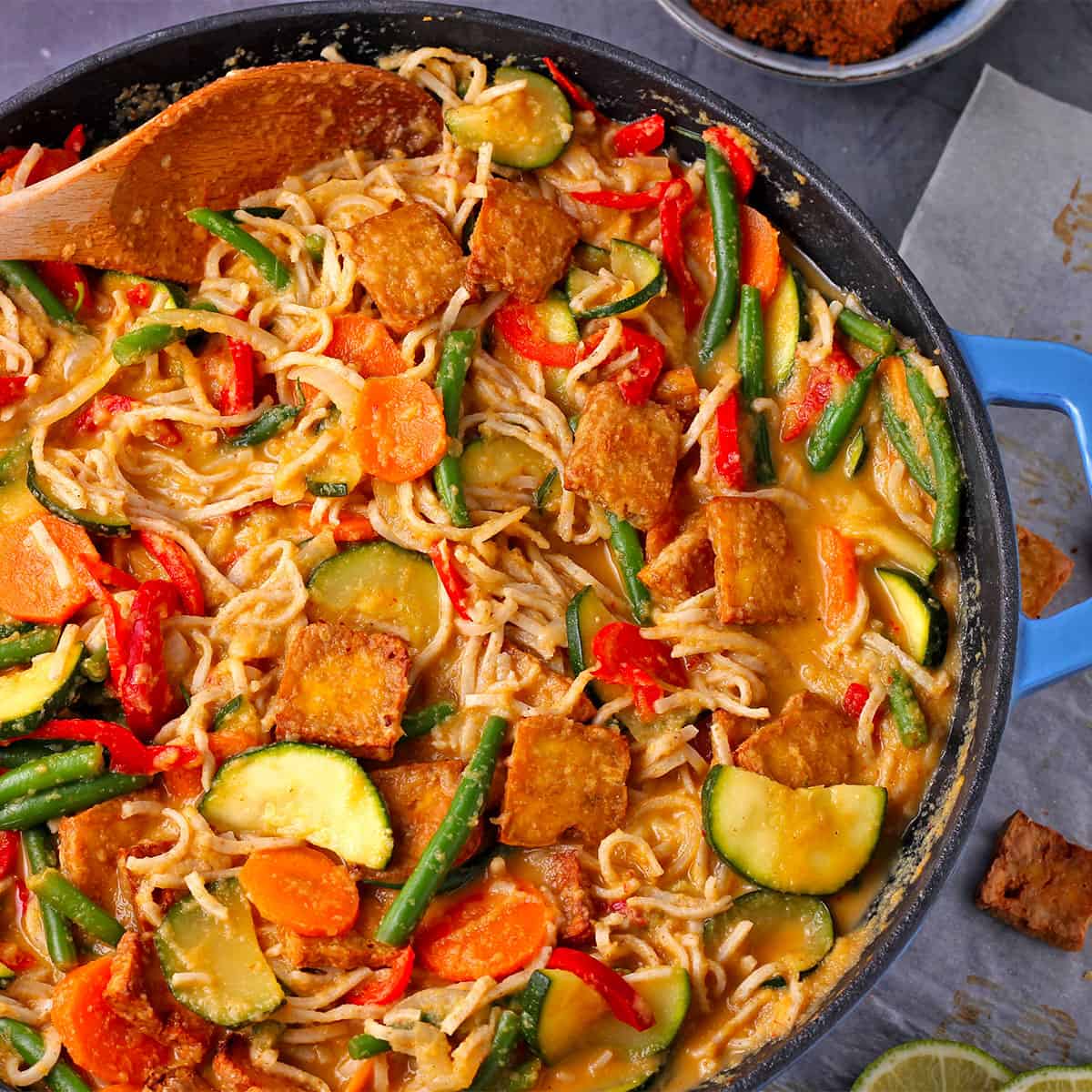 Vegetable mango curry in a skillet with tofu and noodles.