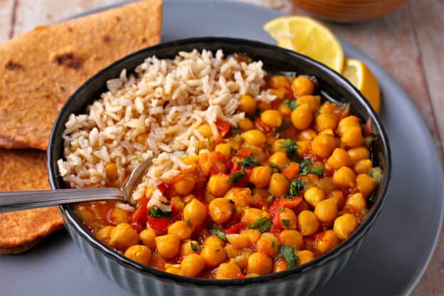 A bowl with chana masala with rice and a spoon.