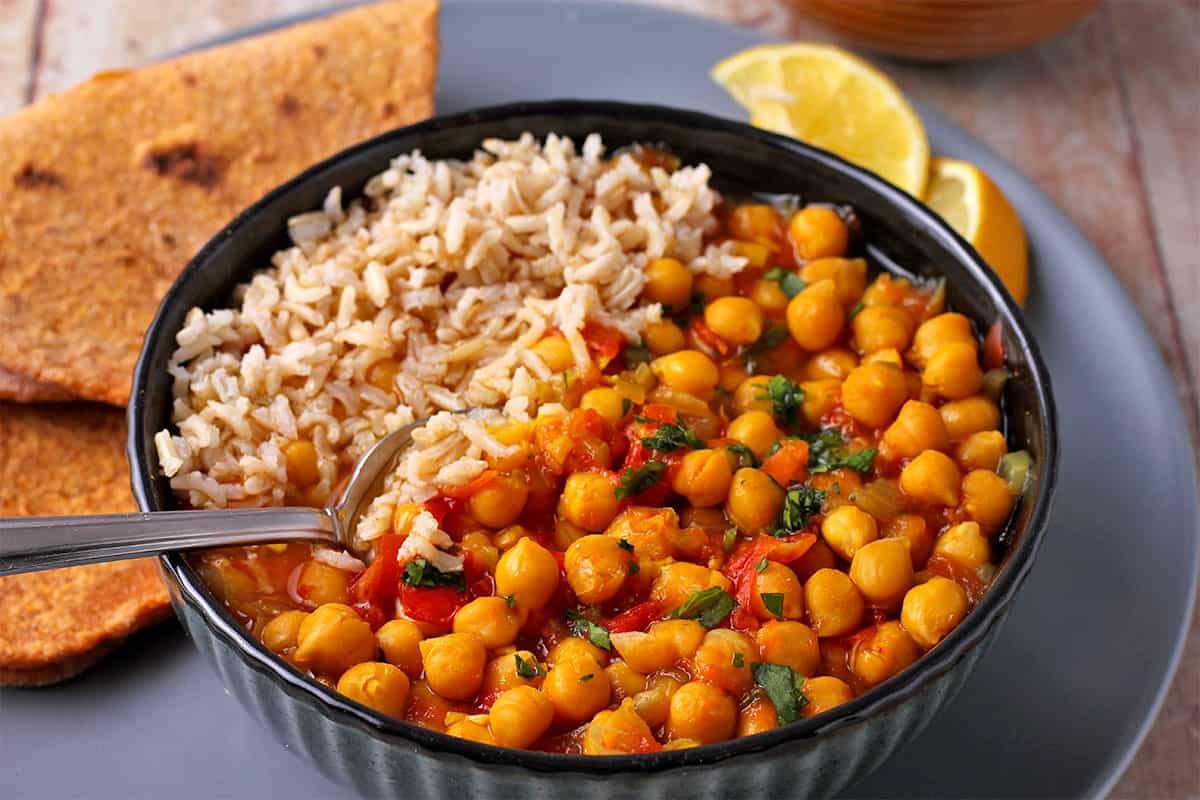 A bowl with chana masala with rice and a spoon.
