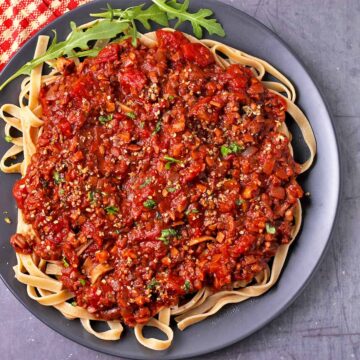 A black plate with pasta and mushroom Bolognese sauce.
