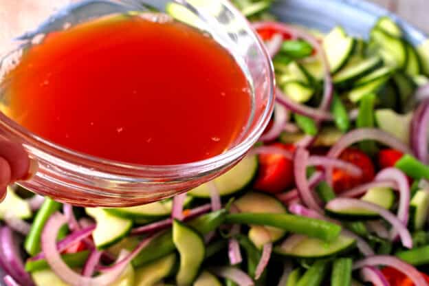 Vinegar dressing is poured over a vegetable salad.