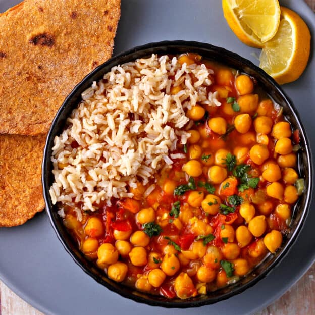 A bowl with rice and chana masala with flatbread on the plate.