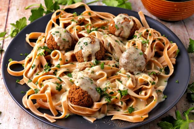 Swedish meatballs with pasta and gravy on a black plate.