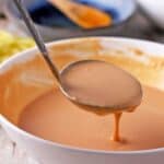 Tahini lime dressing in a white bowl is lifted with a ladle.
