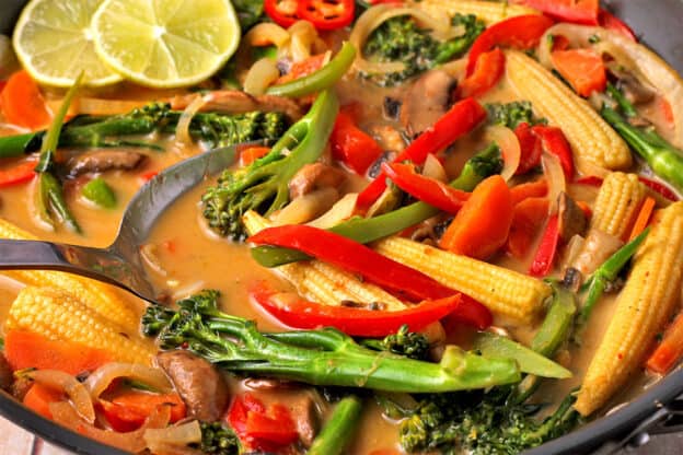 A close up of vegetable red curry in a wok with a spoon.