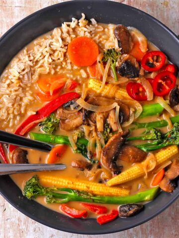 A black bowl with vegetable Thai red curry and rice with flatware in the bowl.