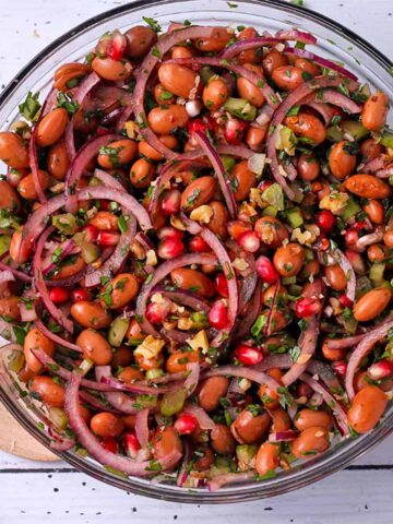 A bowl of Borlotti bean salad with red onions, celery, walnuts, and pomegranate arils.